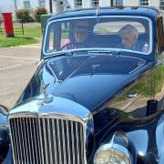 David Holmes (driving, left) takes Norman Rayner (right) for a drive in a Bentley car.