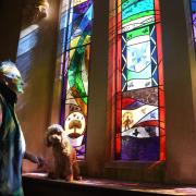 Lance Sharpus-Jones, a churchwarden at St Andrew's church in Thursford, alongside his dog Jazzi, with the newly installed stained glass window at the church. It was designed by some of the villagers